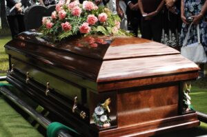 A funeral service with a coffin in place over a grave and mourners gathered around